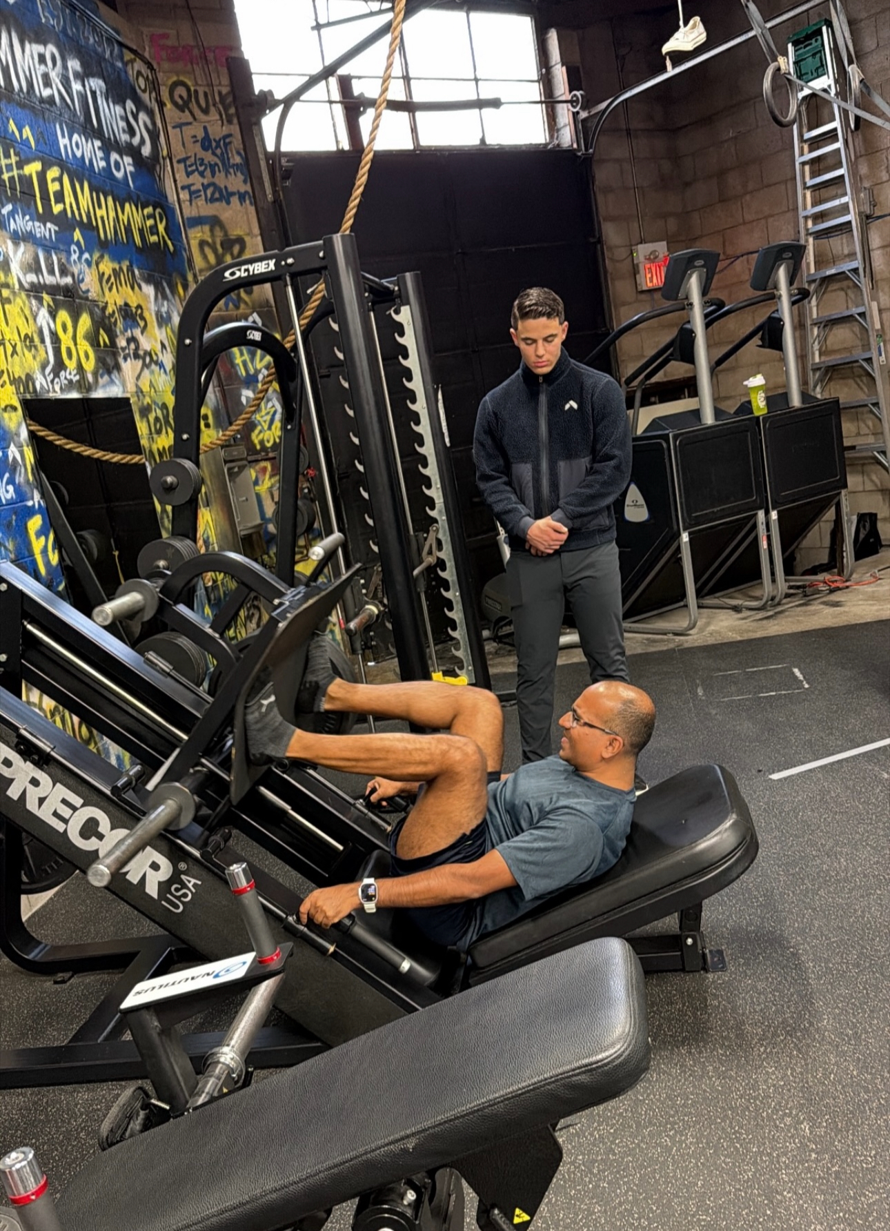 Keyvan Billou supervising a client through a leg press set at Hammer Fitness
